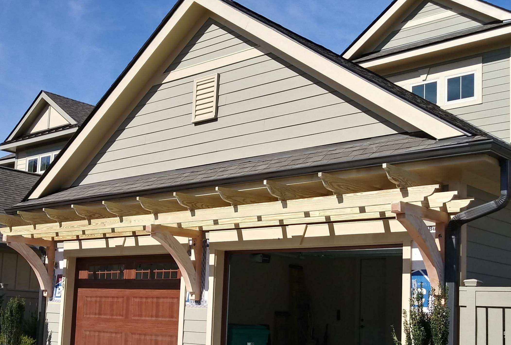 Custom wood pergola with decorative brackets over a garage door Custom wood pergola with decorative brackets over a garage door