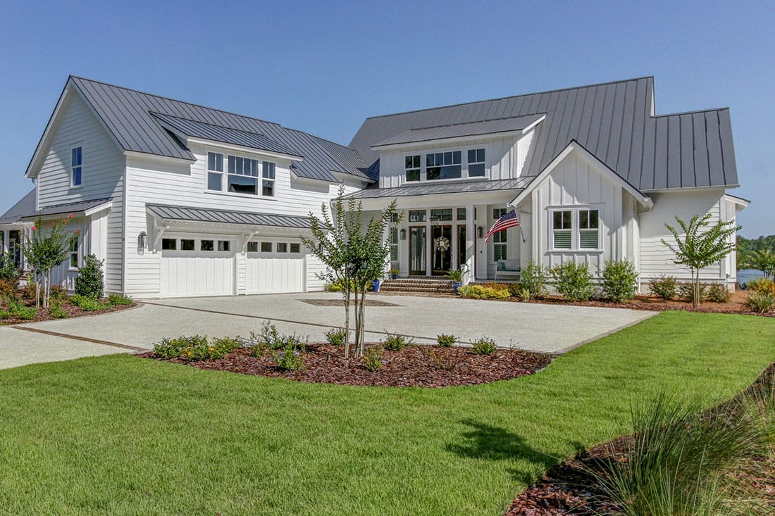 White farmhouse-style home with board-and-batten and lap siding, metal roof, and attached garage White farmhouse-style home with board-and-batten and lap siding, metal roof, and attached garage